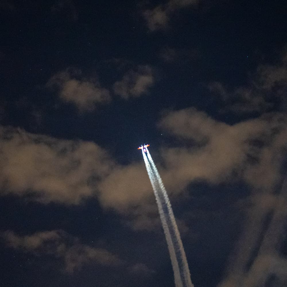 A plane shoots smoke out of its tail end in the cloudy night sky above