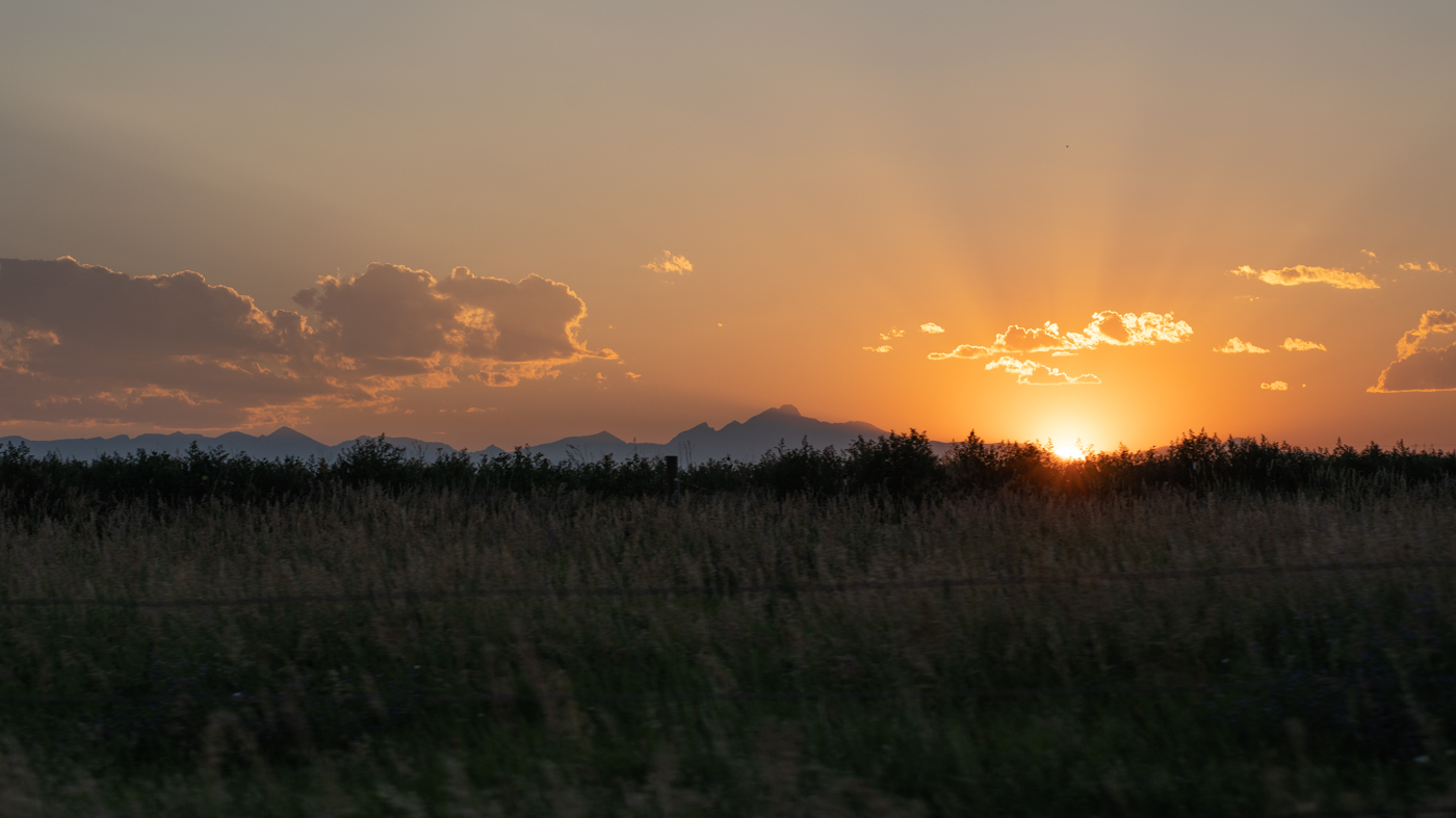 Sunset cresting the Rocky mountains in a hazy bliss in the background, foreground appears to be grass moving quickly past the view