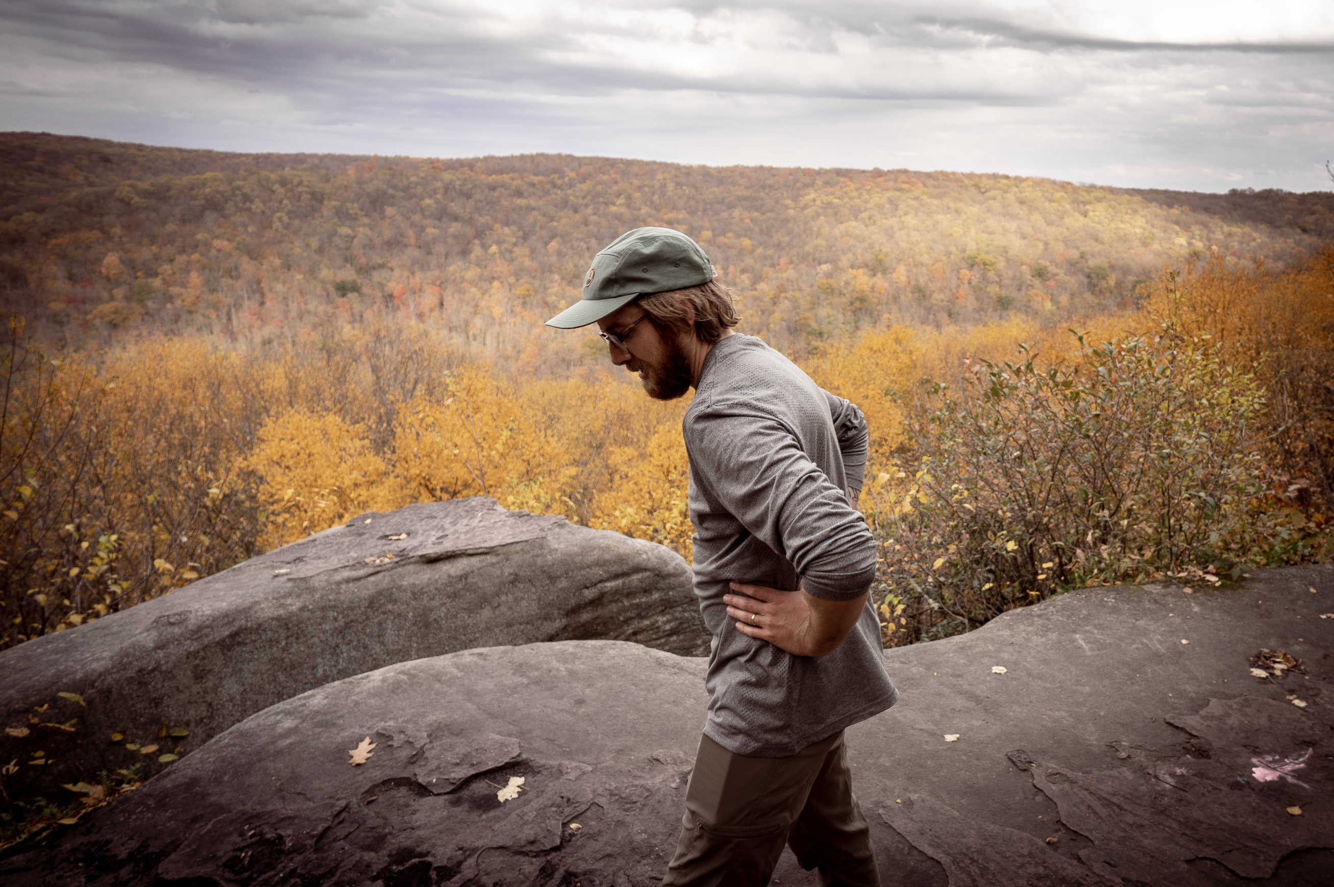 A hiker takes a break atop a boulder overlooking a yellowy-orange fall cannopy in Allegheny National Forest