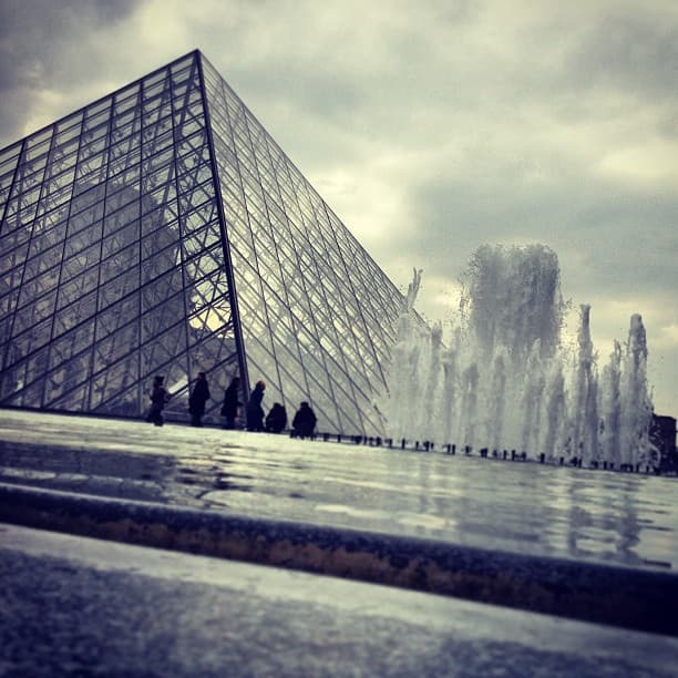 Outisde the Louvre in Paris, glass pyramid and fountain in background